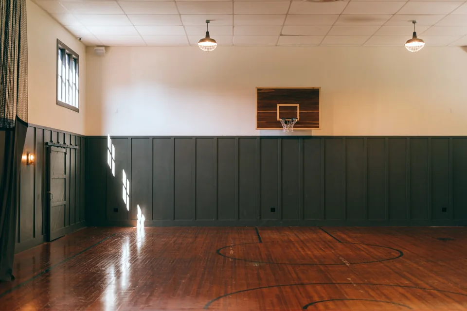 Salle de sport avec parquet, panier de basket et lumière naturelle.