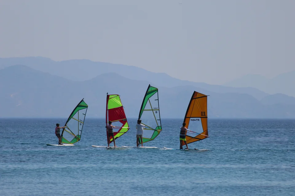 Quatre pratiquants naviguent sur des planches à voile aux voiles colorées.