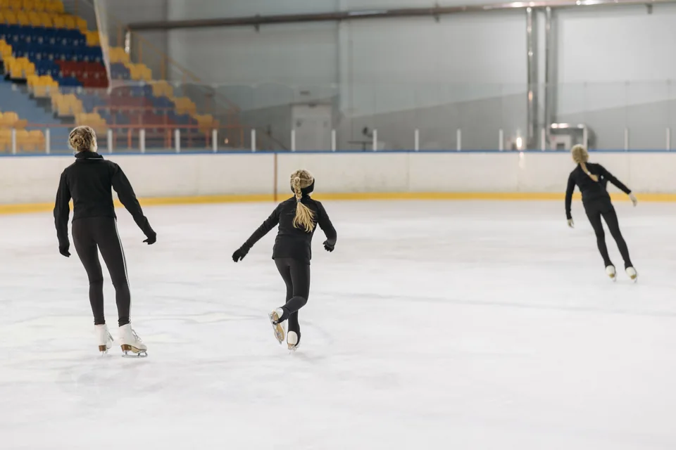 Trois patineuses vues de dos sur la glace d’une patinoire intérieure.
