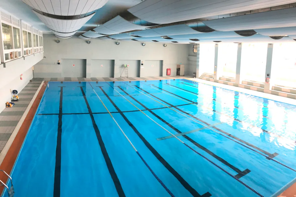 Bassin de natation intérieur avec lignes d’eau, éclairé par de grandes fenêtres.